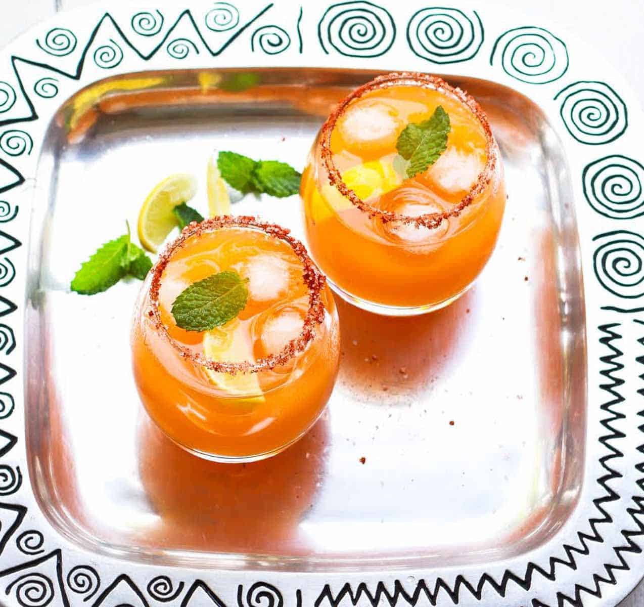 2 glasses of mango margarita with paprika salt on the rims on a tray.