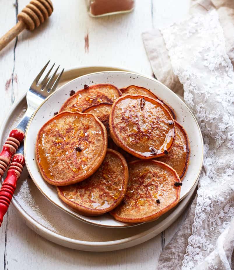 Sourdough pancakes drizzled with honey and stacked on a plate.