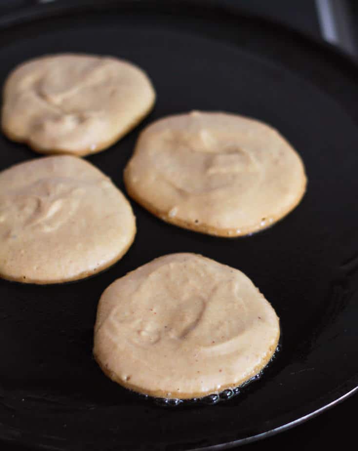 4 small pancakes on a griddle.