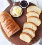 Half a loaf of bread and sliced bread with butter and jam on a board.
