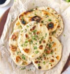 Naans topped with cilantro and nigella seeds on parchment paper.