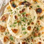 A stack of naan breads topped with onion seeds and cilantro.