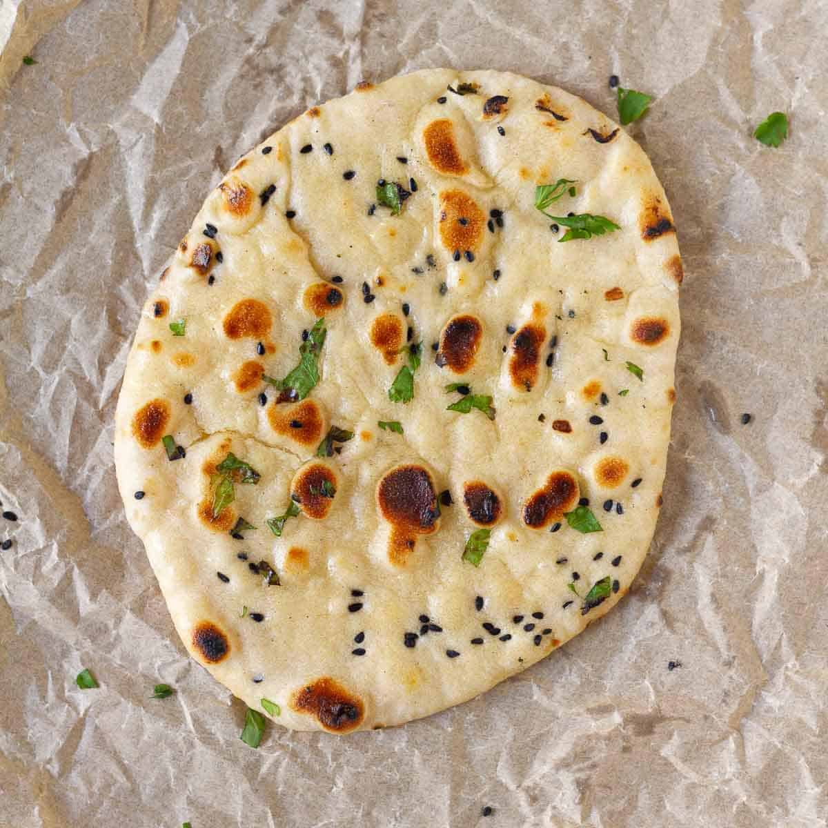 A naan topped with cilantro and onion seeds on parchment paper.