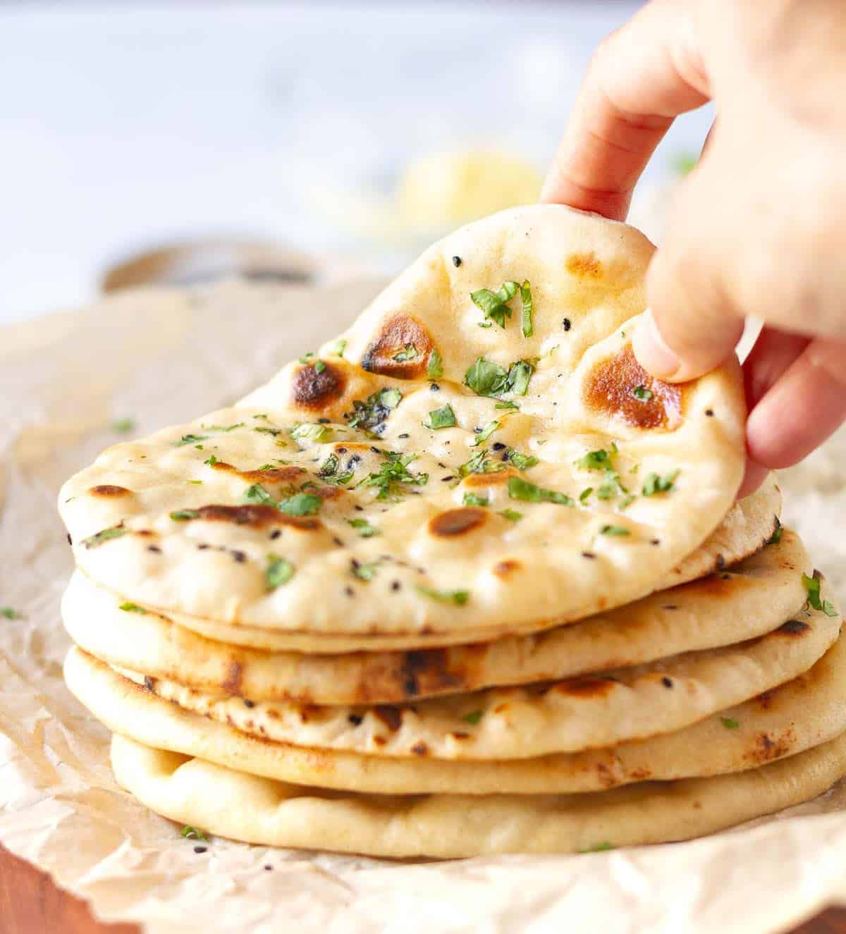A hand picking a naan from a stack of naans.