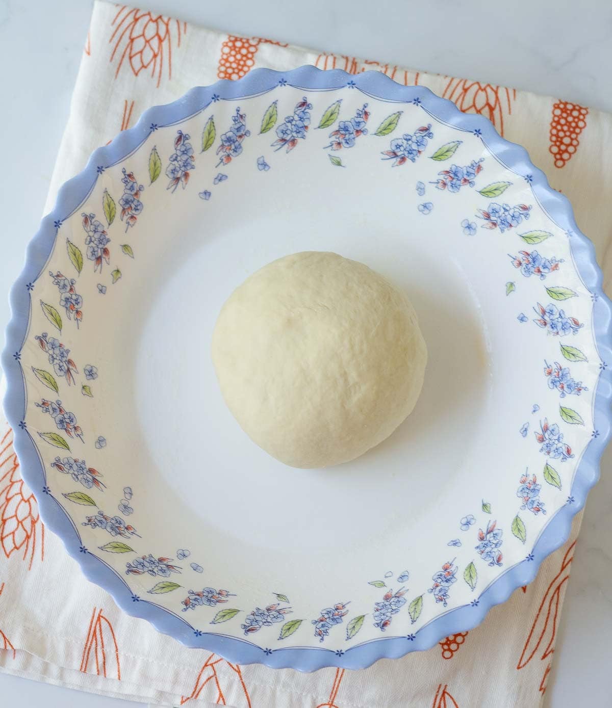 Kneaded dough in a bowl on top of a kitchen towel.
