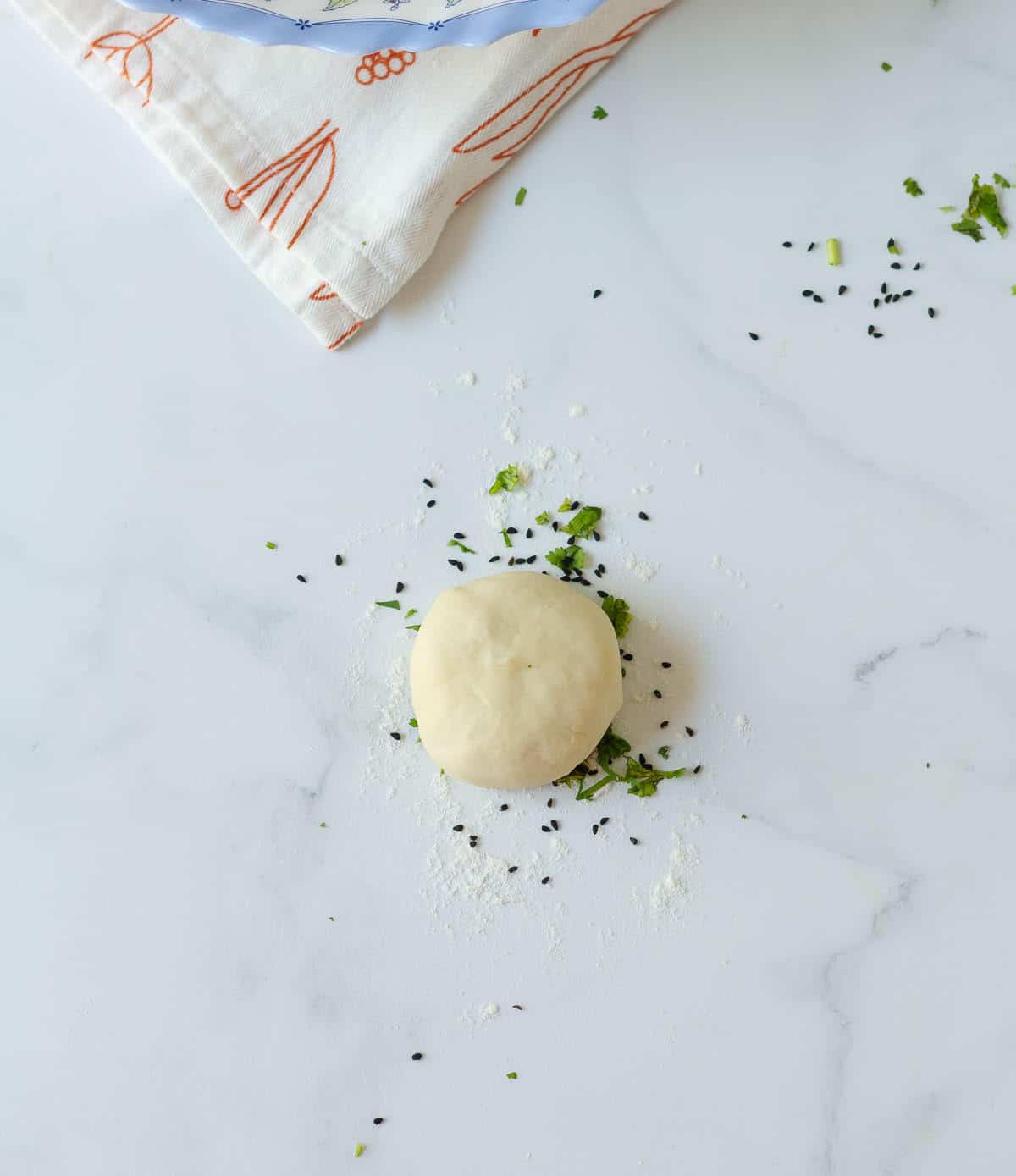 A dough ball placed on a surface sprinkled with cilantro and nigella seeds.