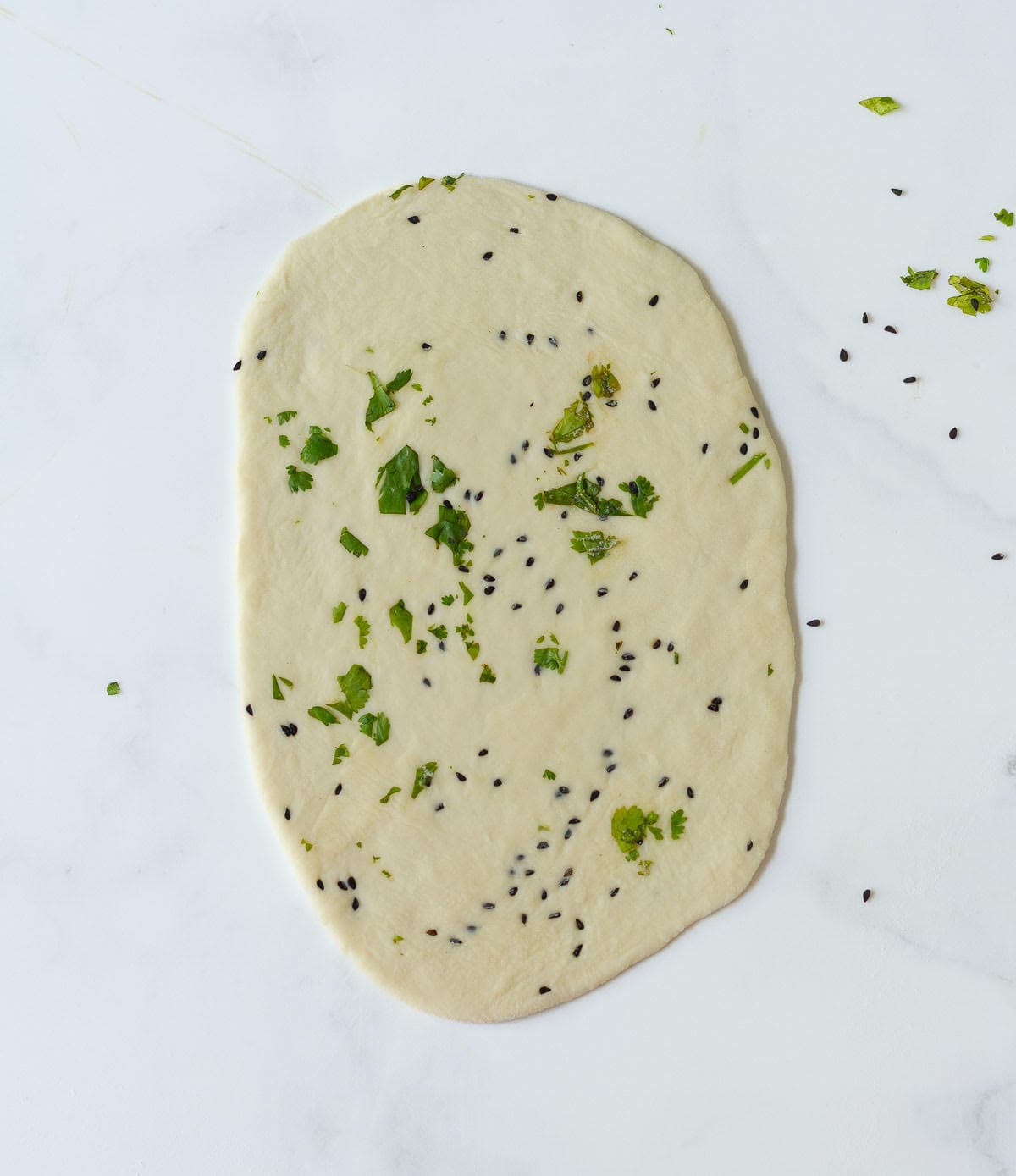Rolled out dough topped with nigella seeds and cilantro.