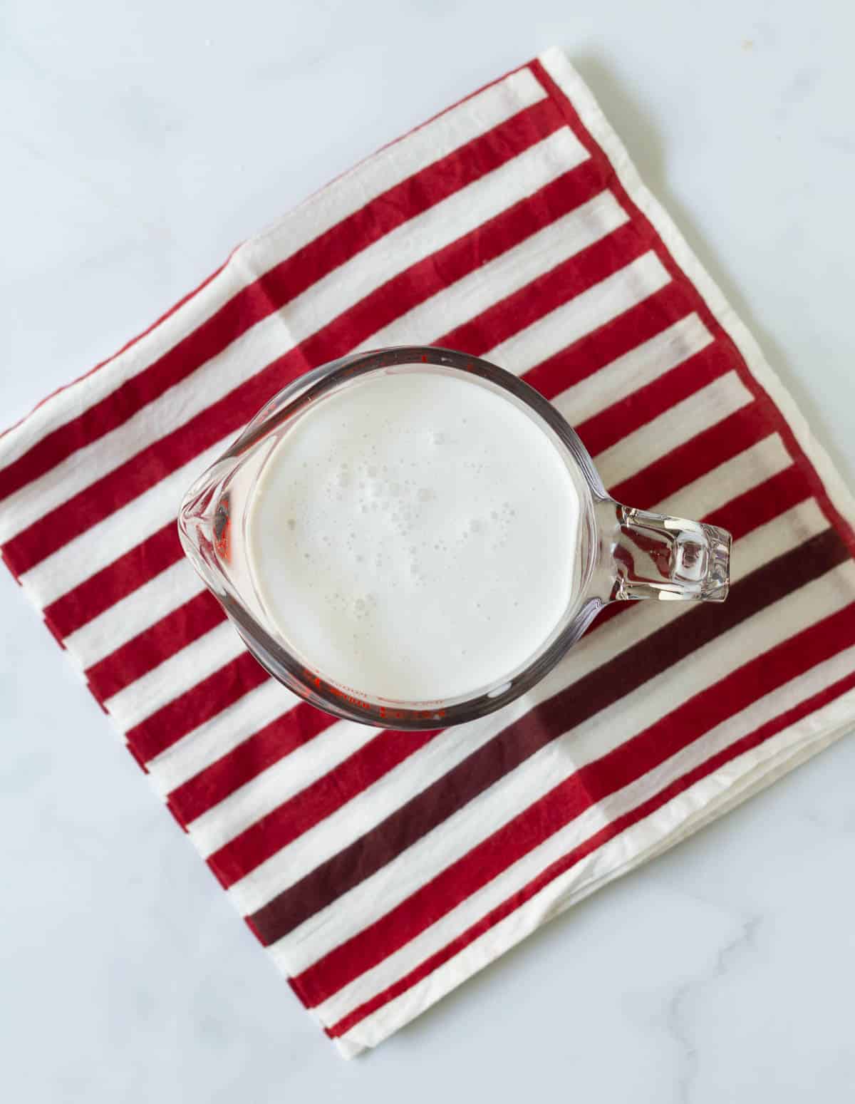 A mixture of milk and vinegar in a glass cup on a striped napkin.