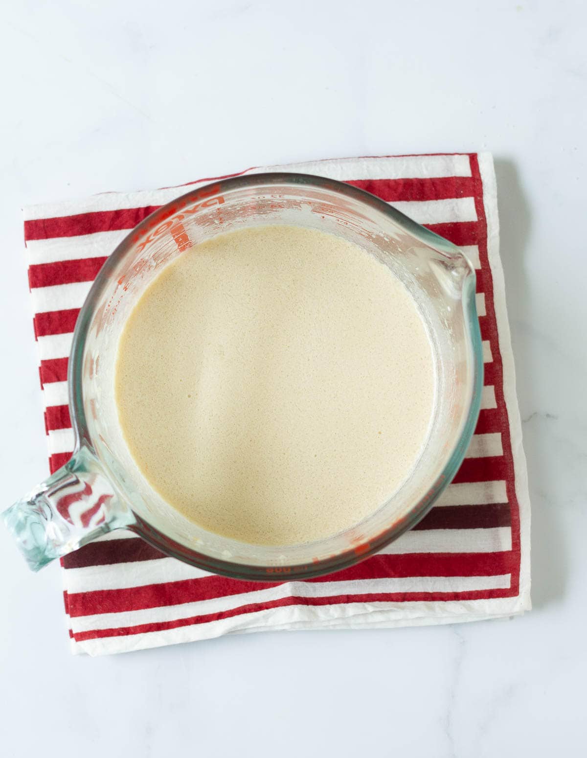 Wet ingredients in a measuring cup on a red striped napkin.