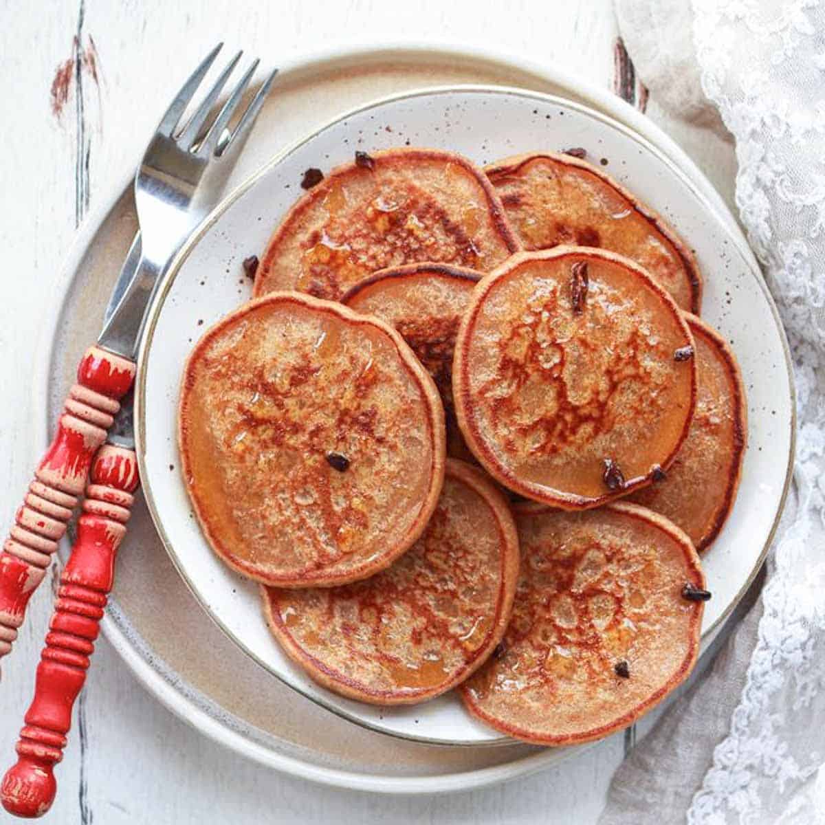 A stack of sourdough banana pancakes on a plate with a fork and knife.