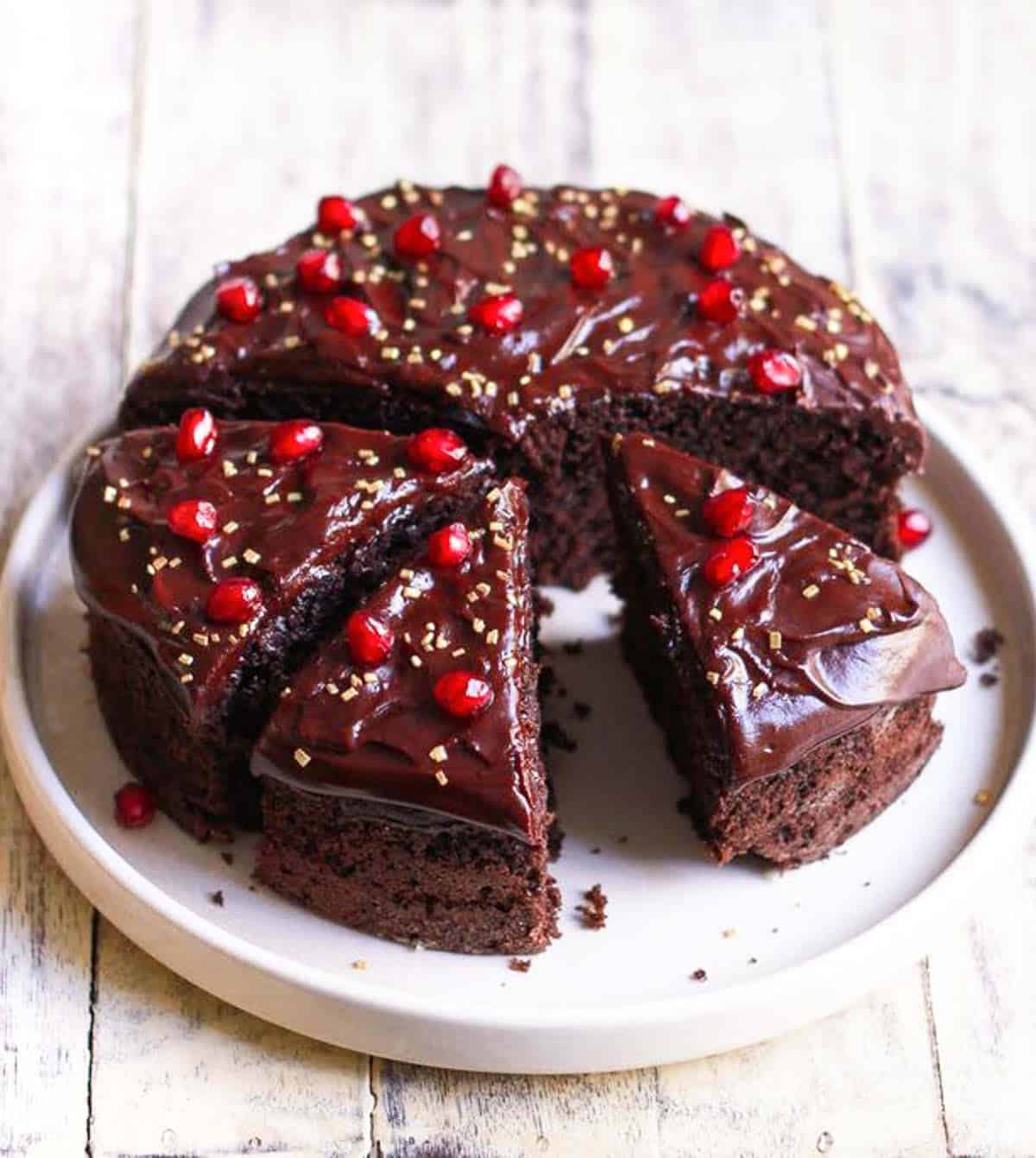 Sliced chocolate cake with chocolate frosting and pomegranates on top on a plate.