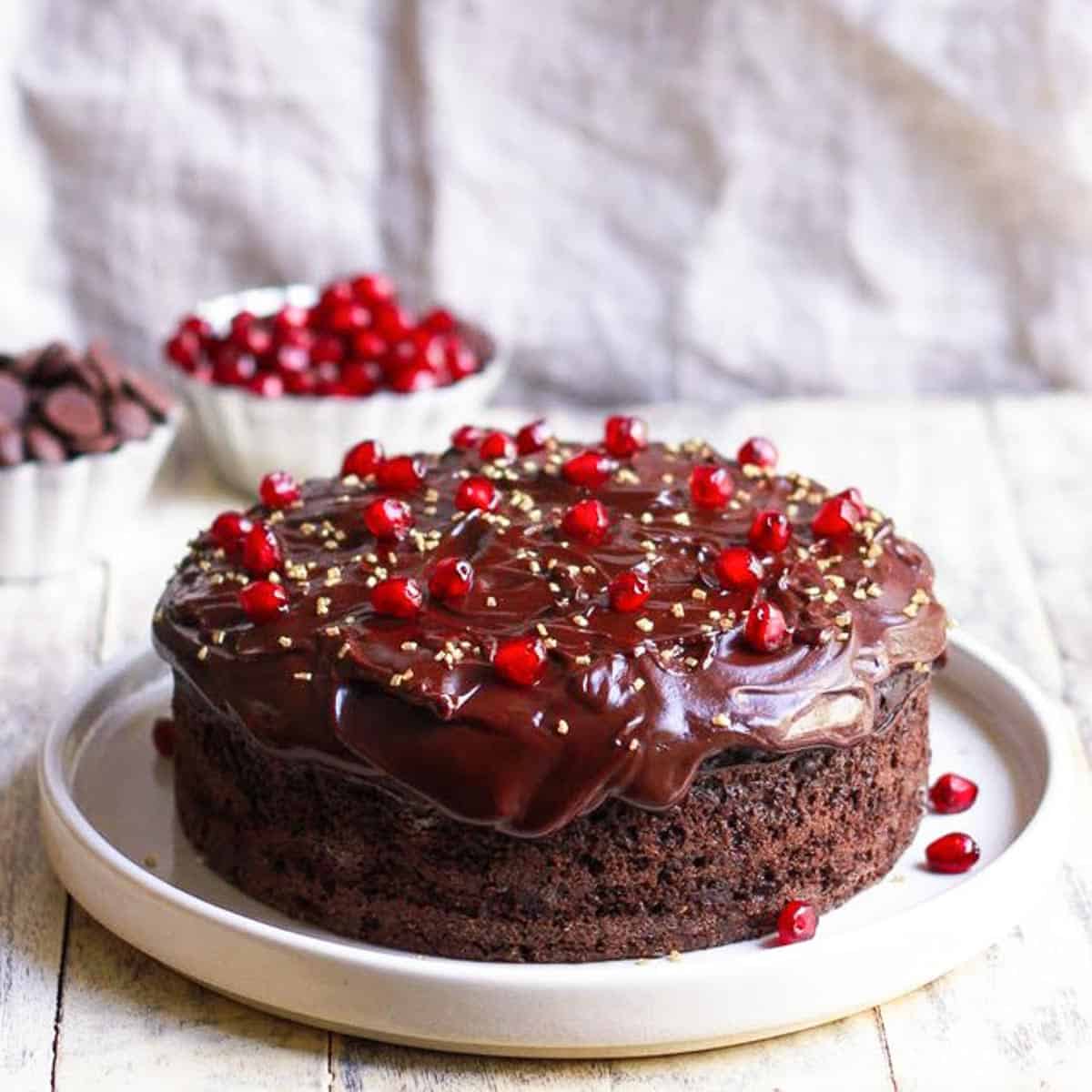 A chocolate cake with frosting and pomegranate arils on a platter.