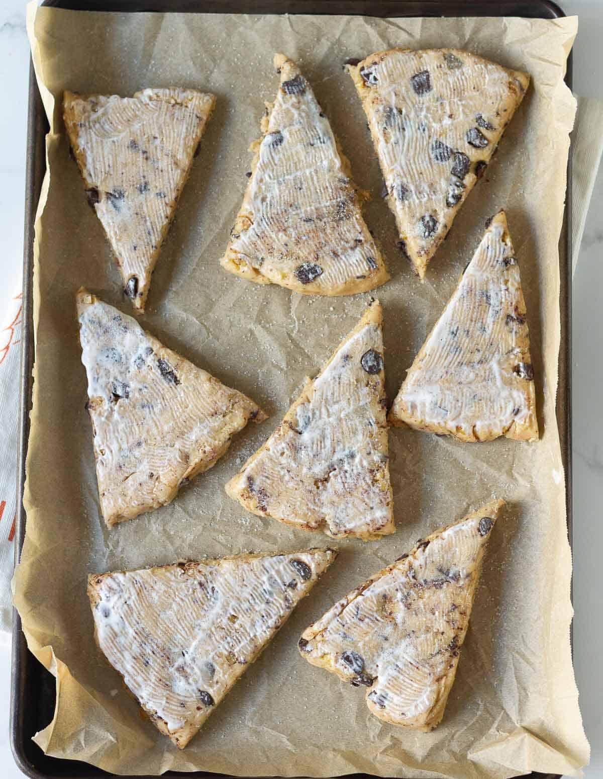 Scones brushed with cream and topped with sugar on a parchment paper lined tray.