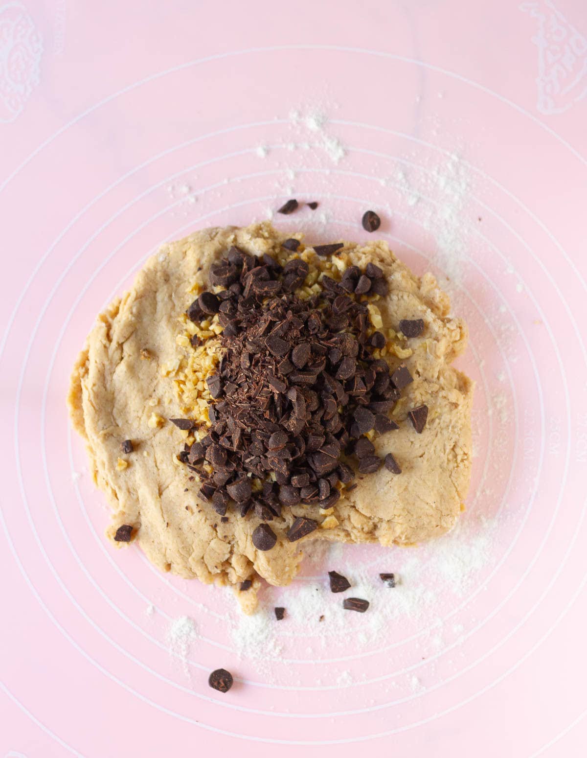 chocolate chips and walnuts on top of dough on a pink silicone mat.