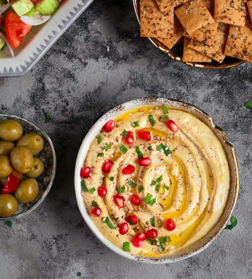 Hummus in a bowl with crackers and olives.