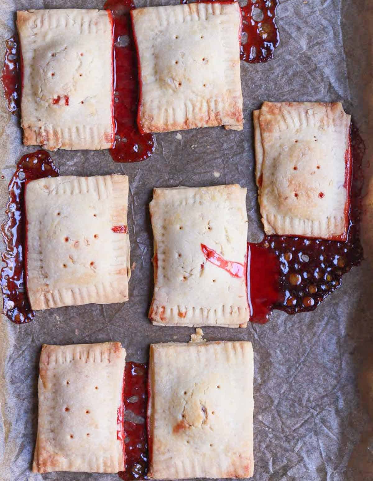 seven baked pop tarts on parchment paper with jam oozing out.