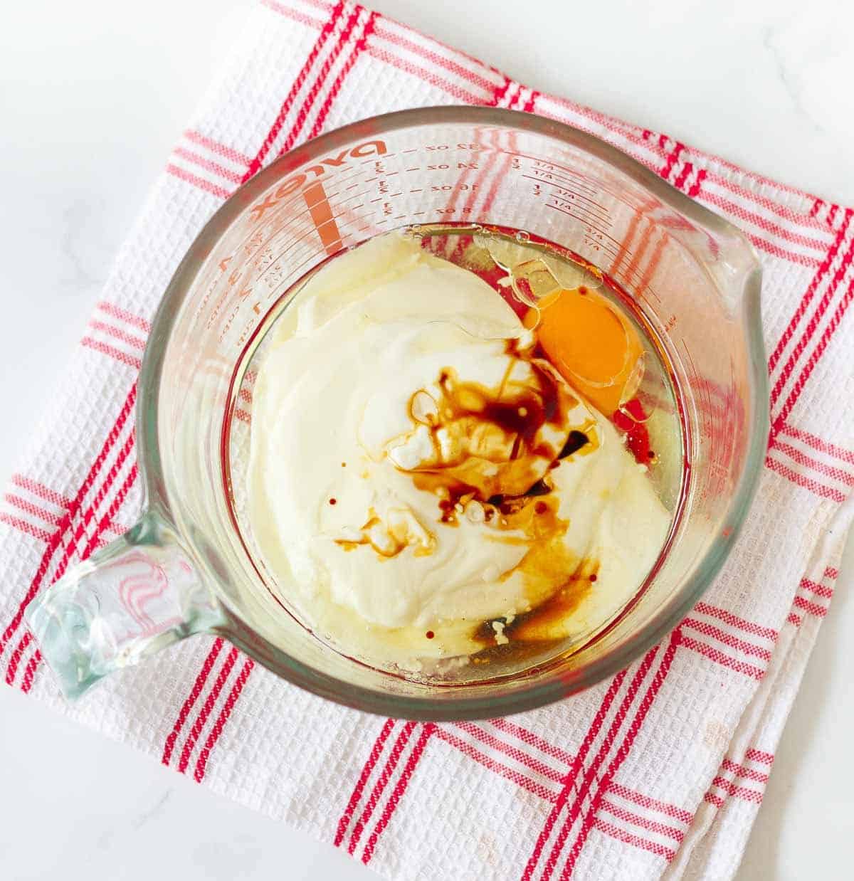Egg, yogurt, oil, vanilla extract, almond extract in a measuring cup.