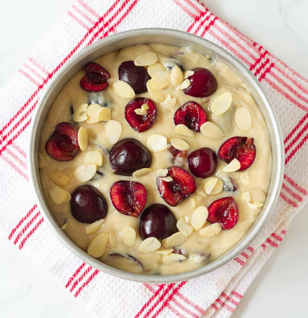 Cake batter with fresh cherries and almond flakes in a cake pan.