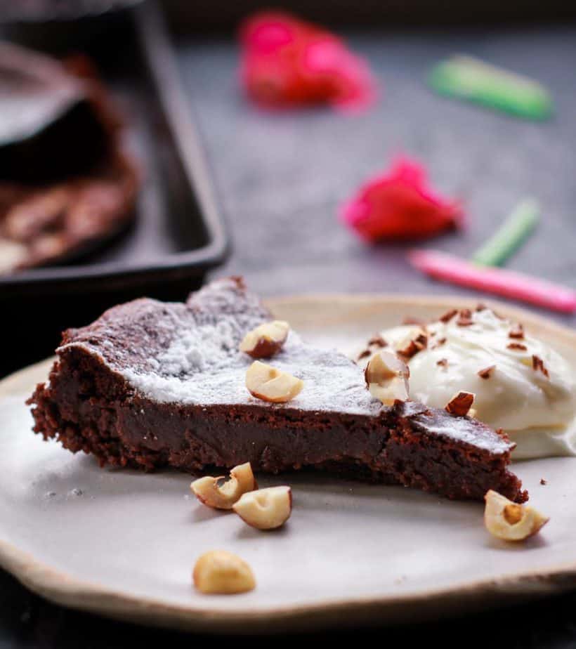 A slice of Swedish kladdkaka with whipped cream on the side on a plate.