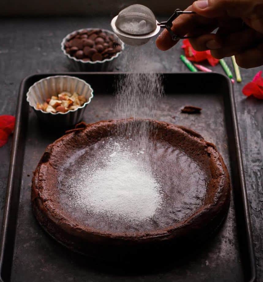 Powdered sugar being sprinkled from a sieve on a chocolate cake.