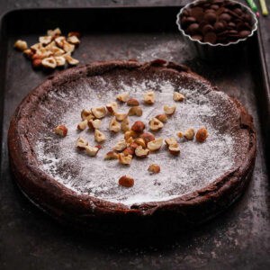 Swedish chocolate cake topped with powdered sugar and hazelnuts on a tray.