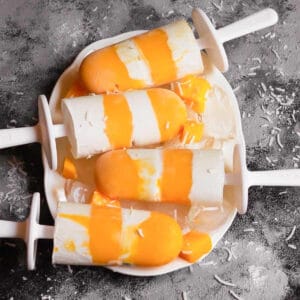 4 mango coconut popsicles on a white tray with ice.