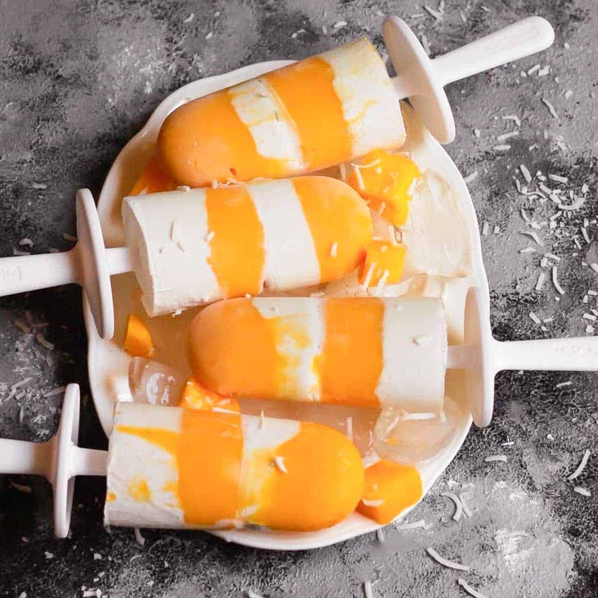 4 mango coconut popsicles on a white tray with ice.