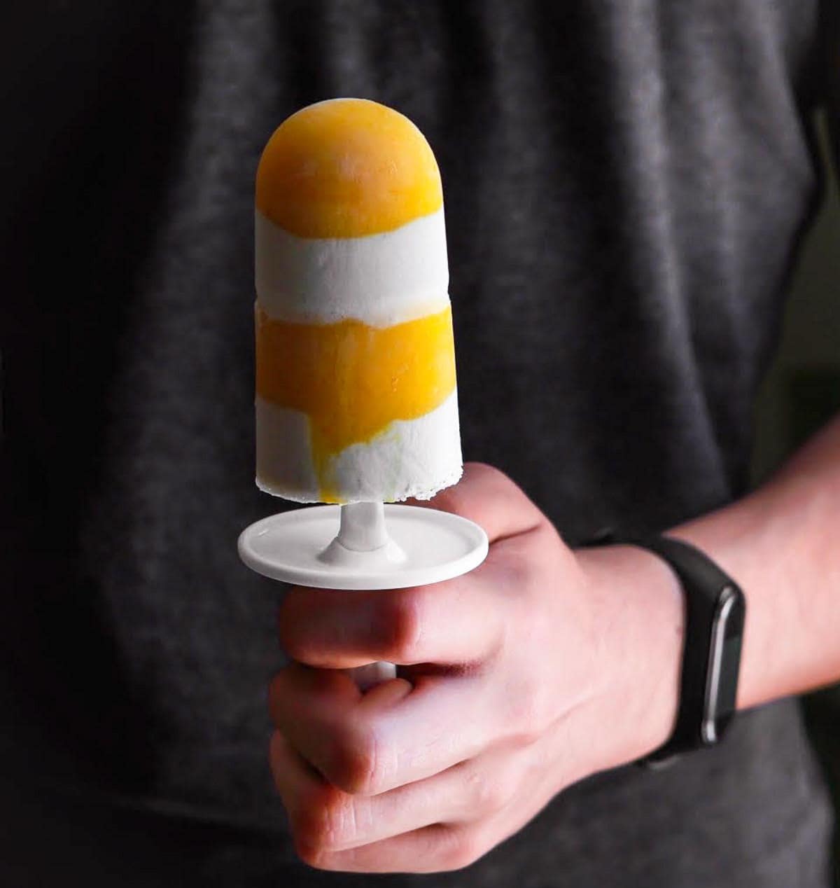 A mango popsicle held in a hand.