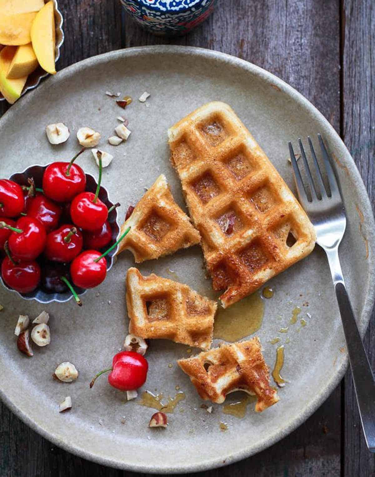 3 bite-sized pieces and half a waffle with maple syrup on a plate.