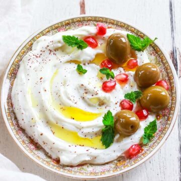 Labneh on a small plate topped with olives,sumac, pomegranate, mint and olive oil.