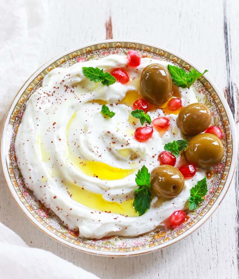 Labneh on a small plate topped with olives,sumac, pomegranate, mint and olive oil.
