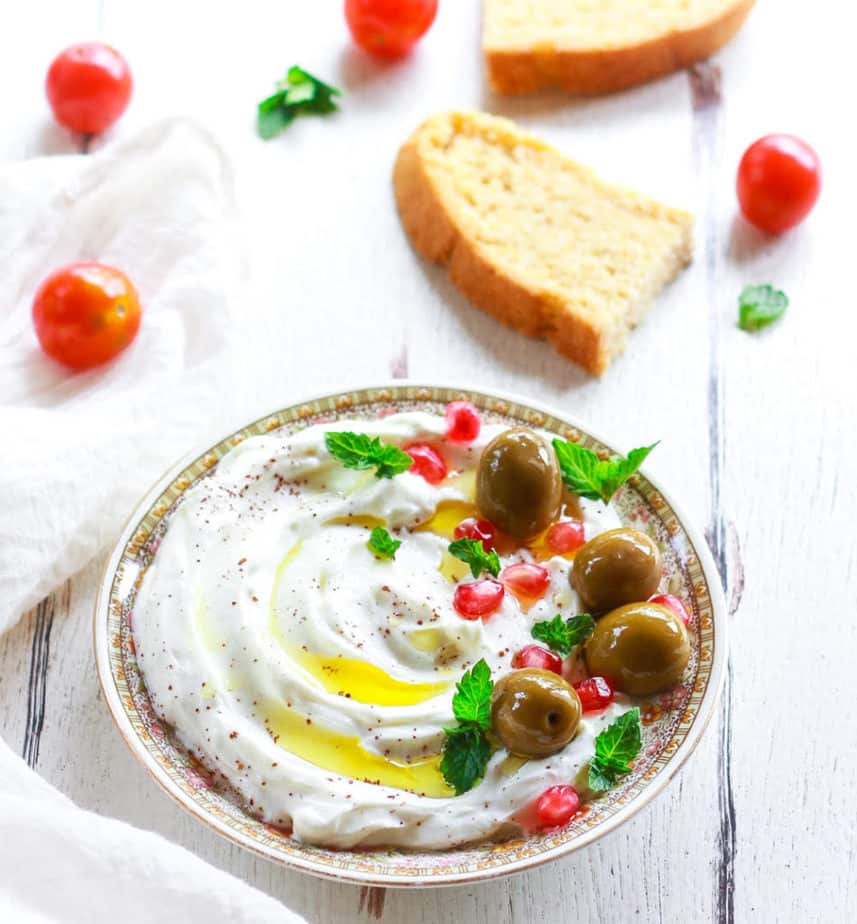 Homemade labneh on a plate, topped with olives, pomegranate, mint, sumac and olive oil.