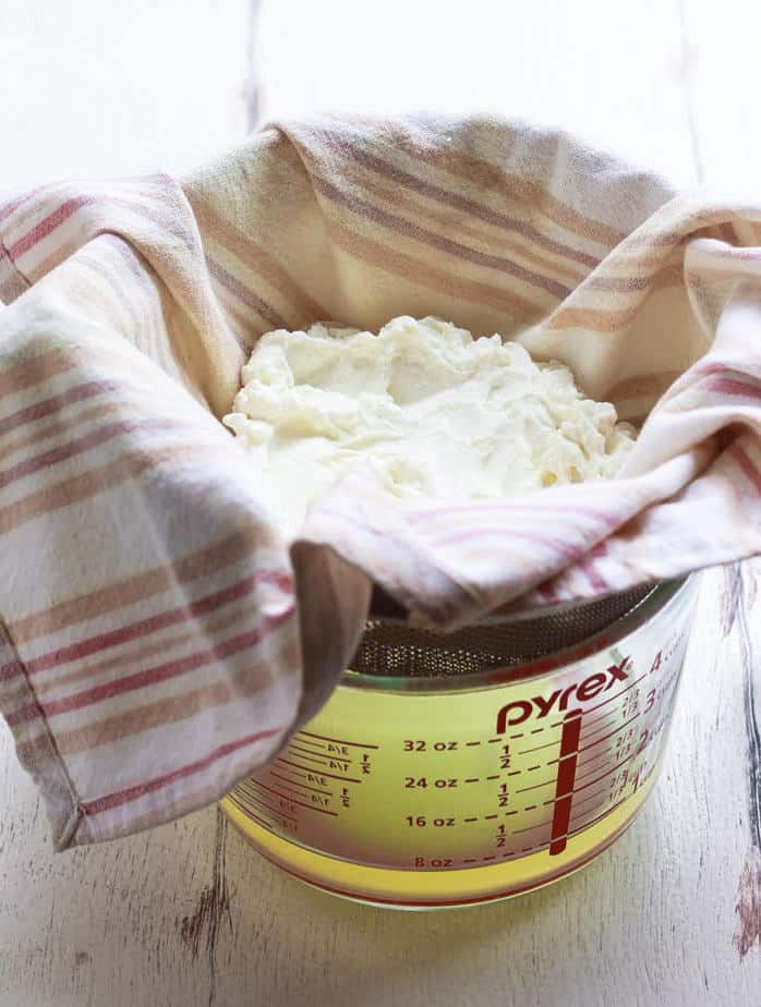Yogurt on a kitchen towel placed over a sieve over a measuring cup with whey.