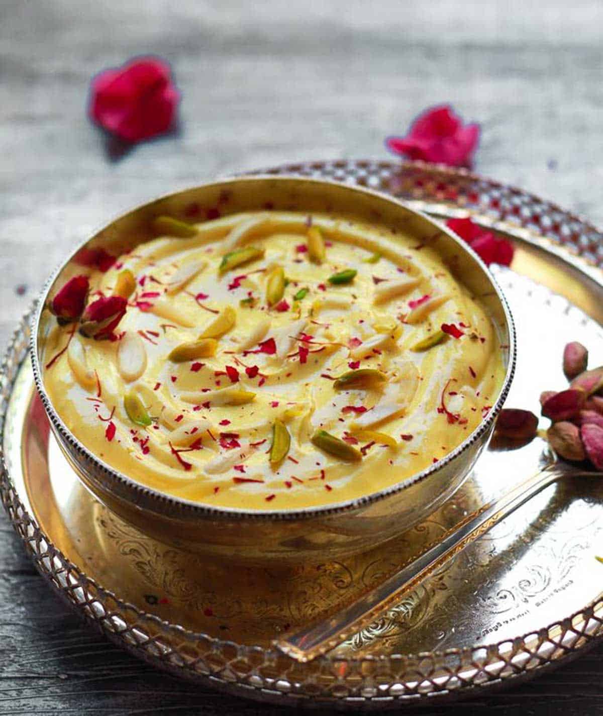 mango shrikhand in a silver bowl garnished with rose petals, pistachios and almonds.