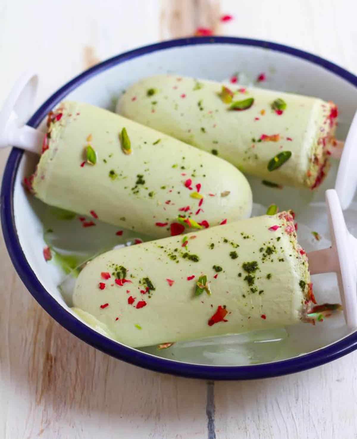 3 matcha popsicles in a white tray with ice.