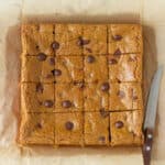 A bar of coffee blondies cut into squares with a knife on the side.