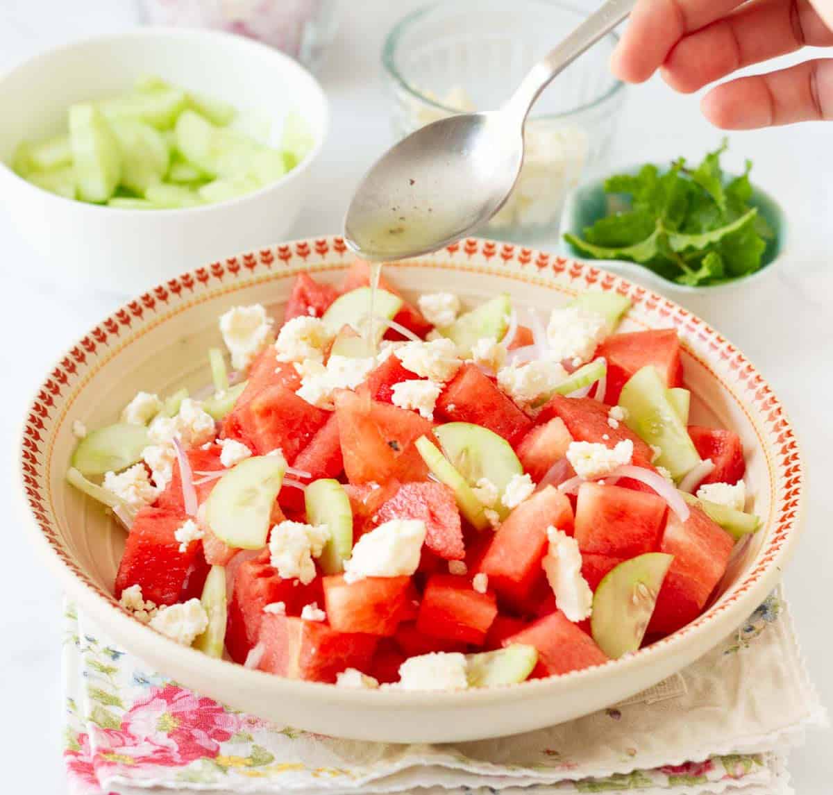 A hand holding a spoonful of dressing on top of watermelon salad.
