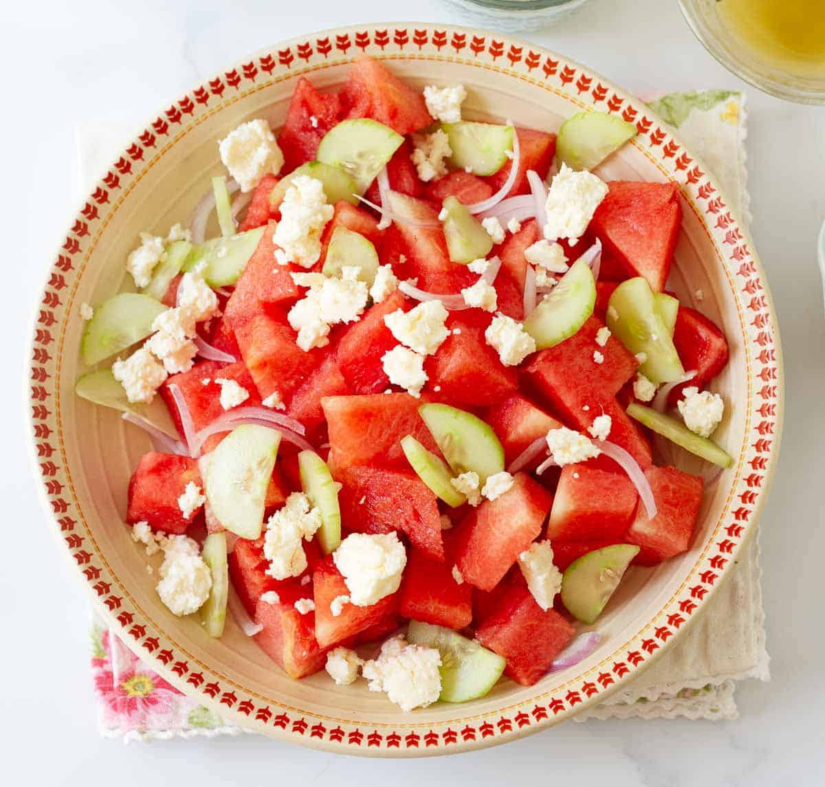 Chopped watermelon, onions, cucumber, and crumbled feta cheese in a bowl.