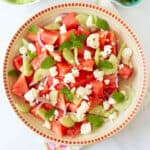 A bowl of watermelon salad with onions, cucumbers, mint, and feta cheese.