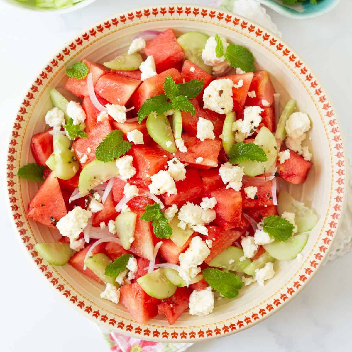 A bowl of watermelon salad with onions, cucumbers, mint, and feta cheese.