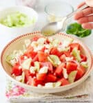 A hand holding a spoonful of dressing on top of watermelon salad.