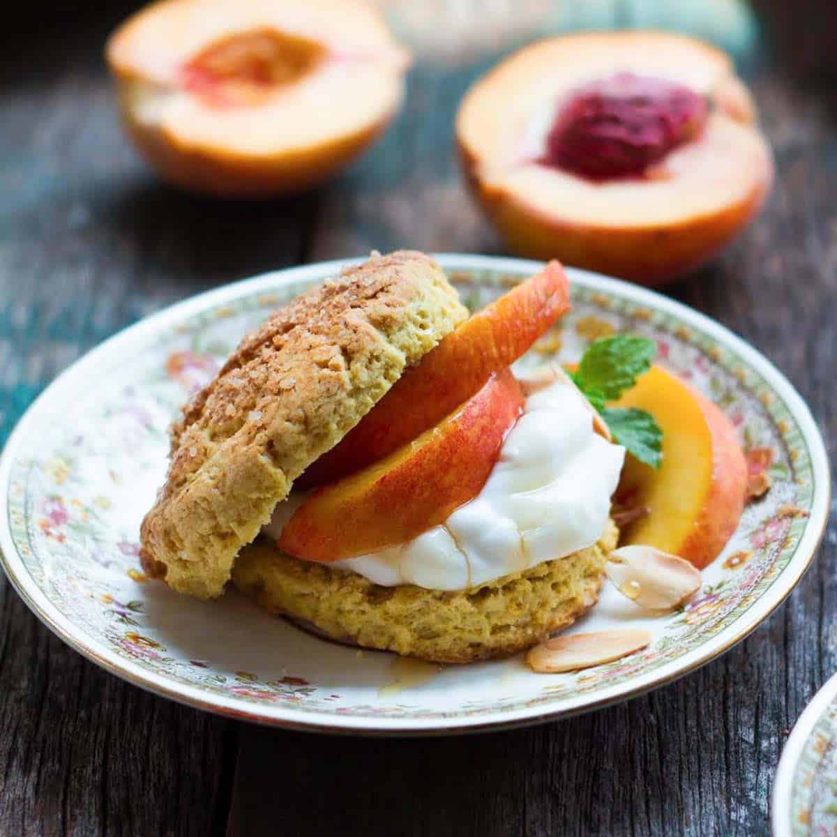 A shortcake split in half and filled with peaches and whipped cream on a plate.