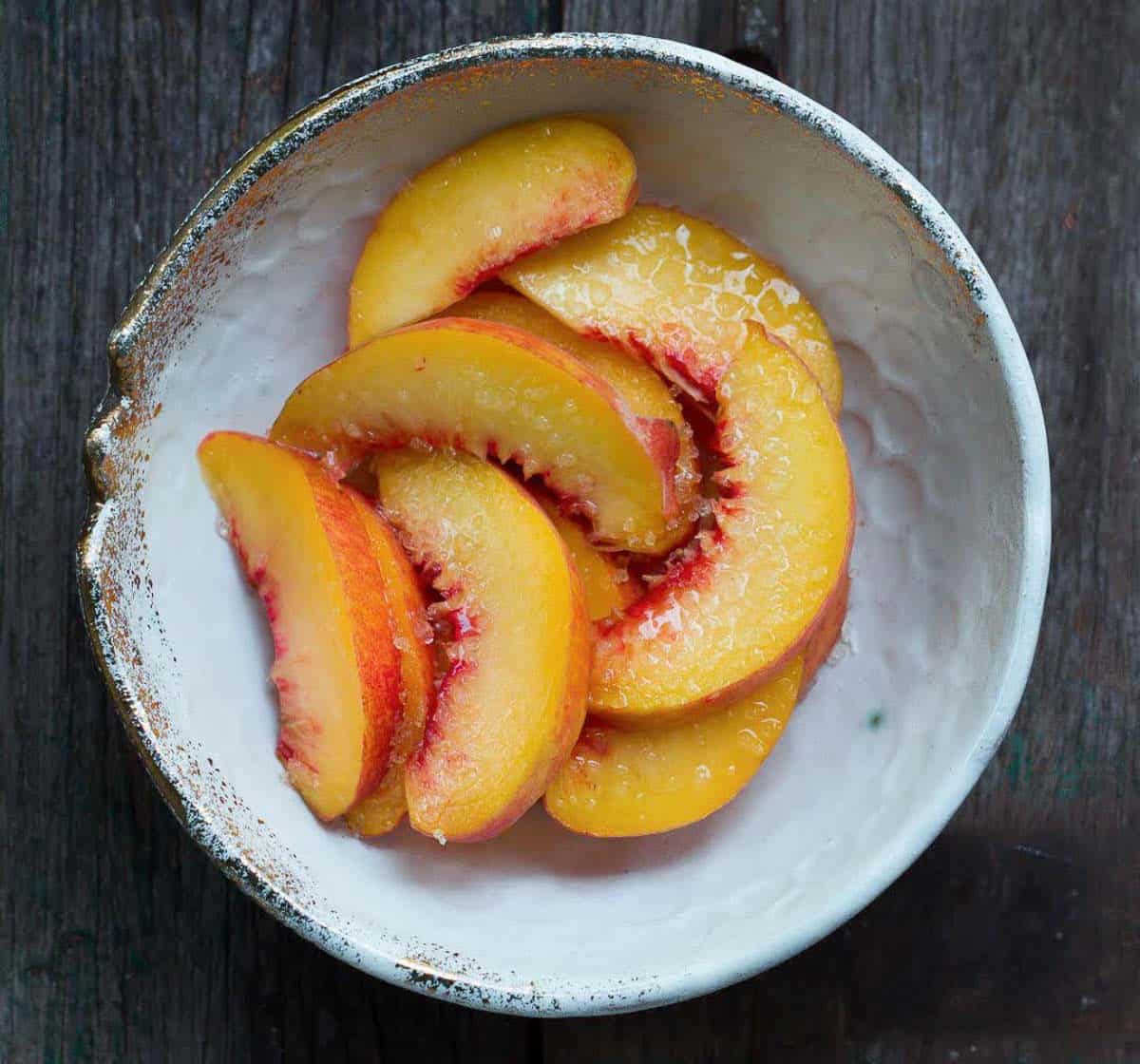 Sliced peaches tossed with sugar in a bowl.