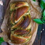 Braided pesto bread on parchment paper with ingredients around.