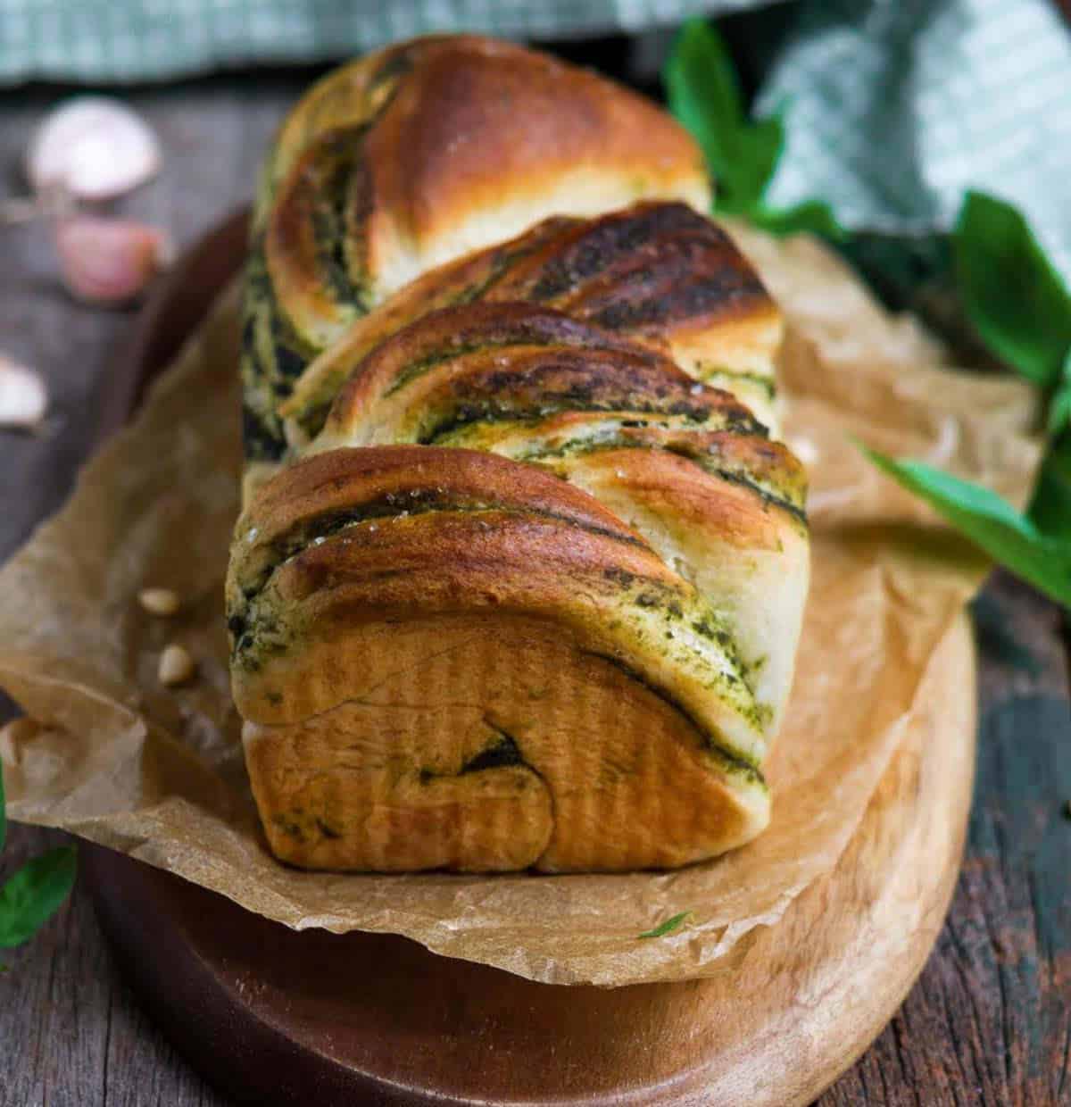 Baked pesto bread on a wooden board with ingredients around.