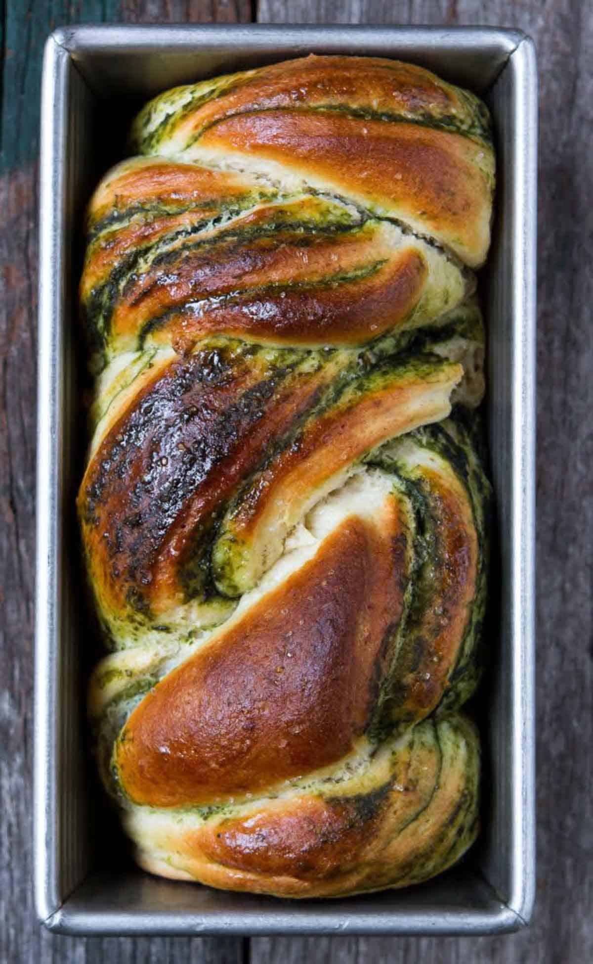 A loaf of braided pesto bread in a baking pan.