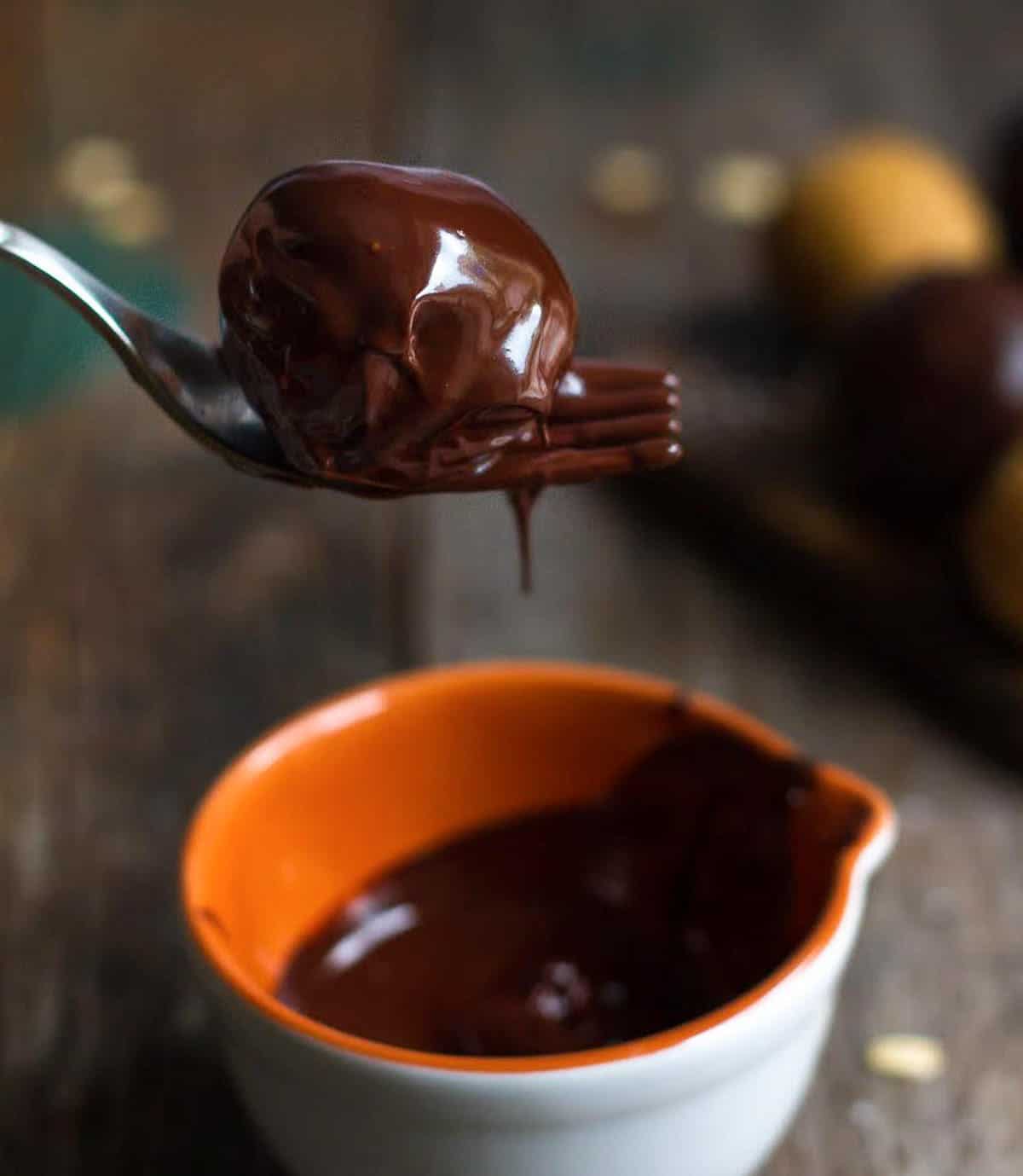 A chocolate covered ball on a fork on a bowl of melted chocolate.