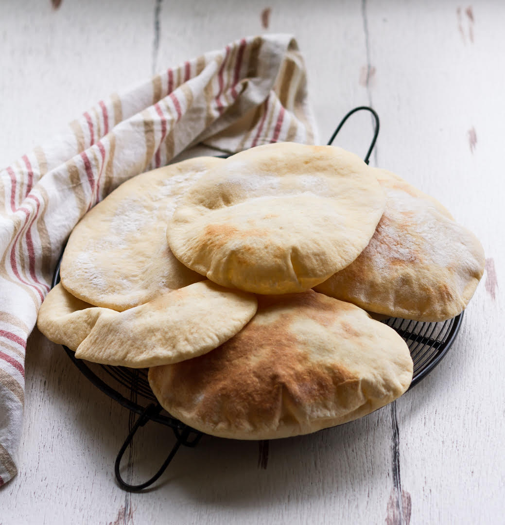 Stacked pita bread on a metal trivet with a kitchen towel.