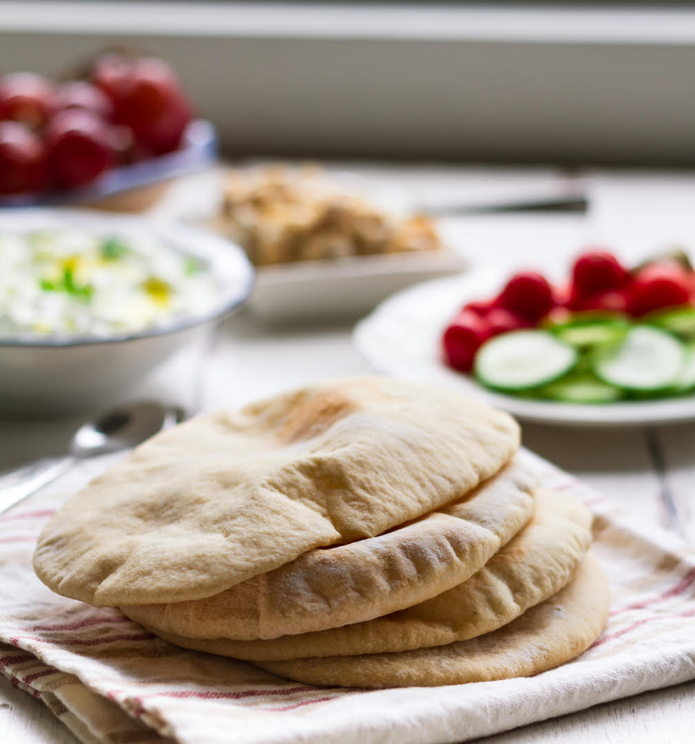 Pita Breads stacked on a kitchen towel with dips and salads in the background.