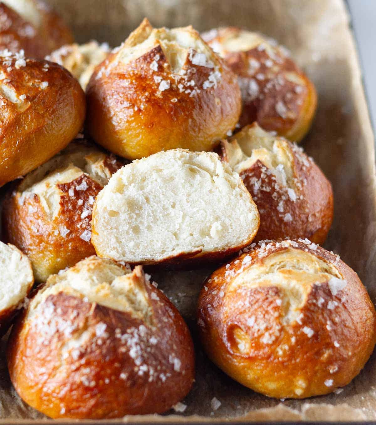 Pretzel buns on a tray with one bun cut into half to show the texture.